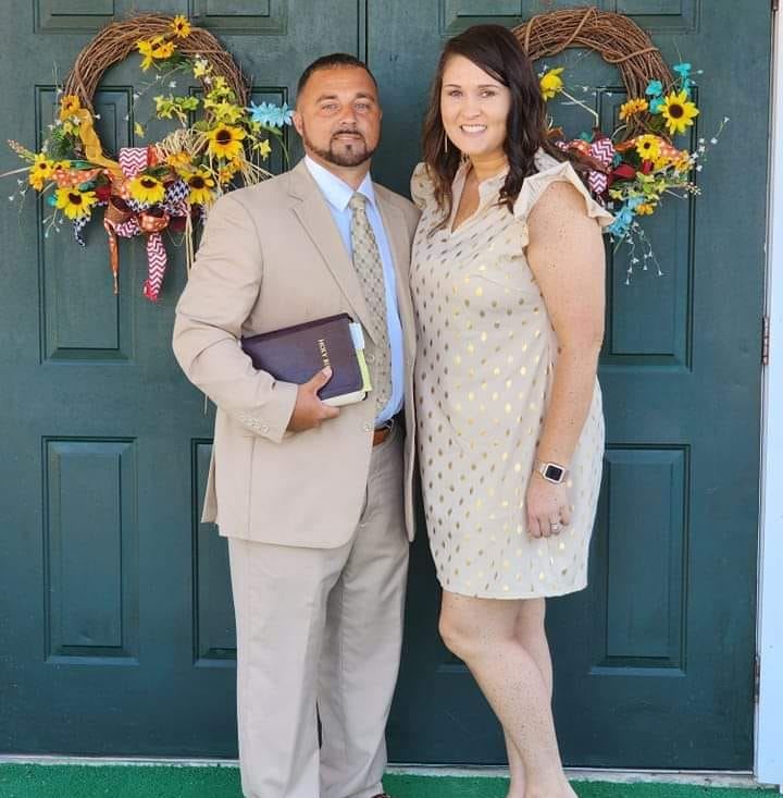 A well-dressed couple standing together in front of double doors decorated with sunflower wreaths.